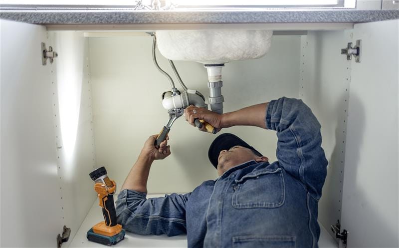 Plumber repairing pipes beneath a bathroom sink in Crestview