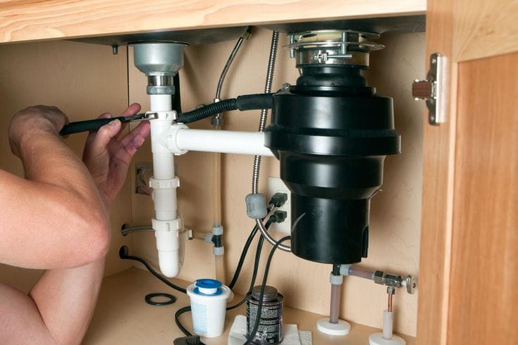 Plumber installing a garbage disposal beneath a kitchen sink in Crestview