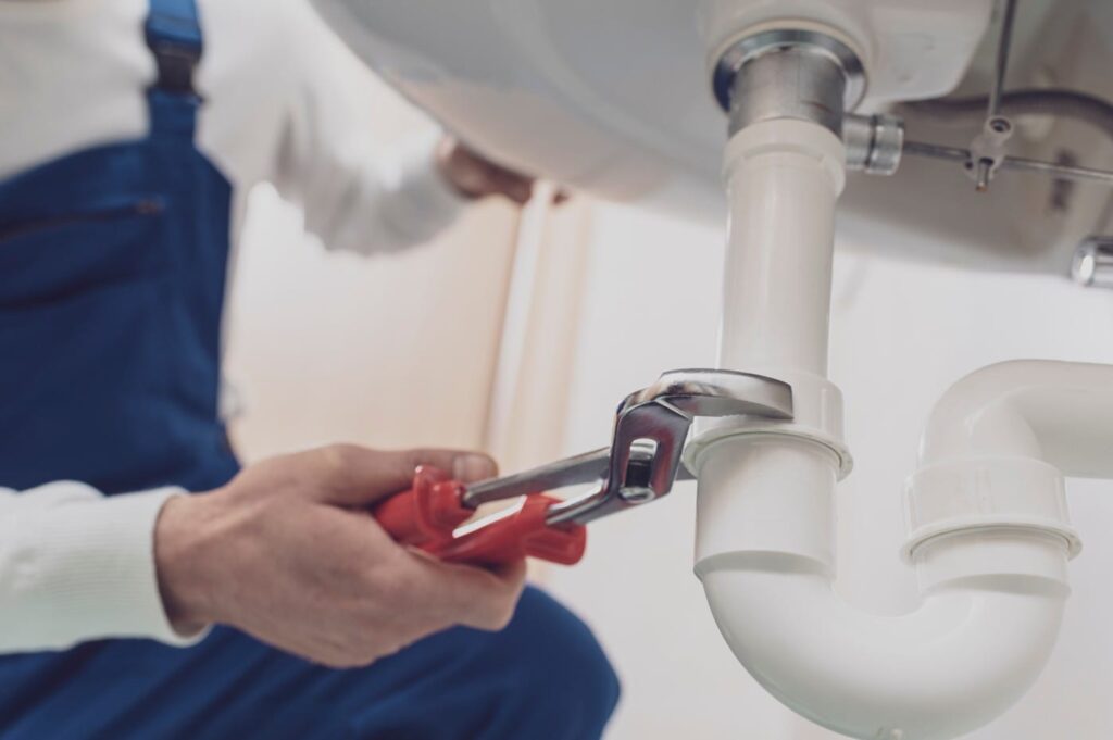 Plumber repairing a white drain pipe beneath a sink in Crestview