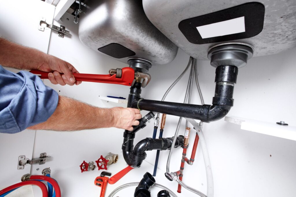 Plumber repairing drain pipes beneath a kitchen sink in Crestview